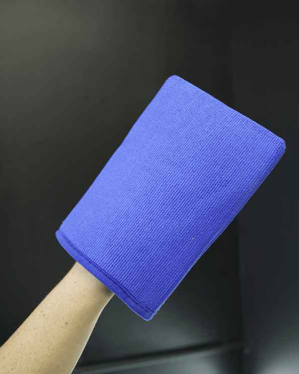 A person holding a blue clay mitt on a dark background