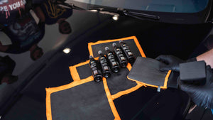 3 clay cloths on a black car bonnet with bottles on top