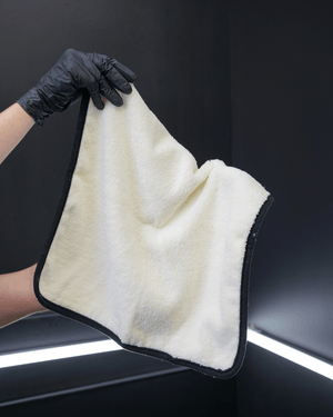 A person holding a plush white microfibre towel with a black border in a car detailing bay
