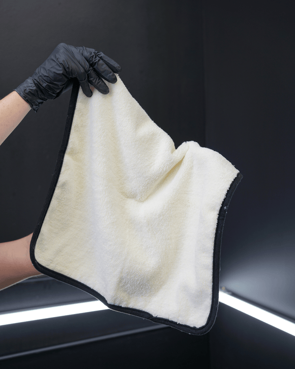 A person holding a plush white microfibre towel with a black border in a car detailing bay