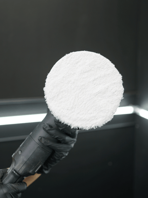 Buffing machine with a white foam cover held by a person wearing black gloves against a dark background