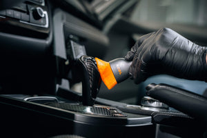 ADBL detailing brush with orange bristles cleaning a carbon fibre gear shift and car interior trim