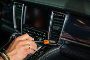 Detailer using orange and black ADBL Detail Brush to clean dust from car air vents and dashboard