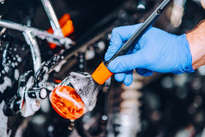 Hand in blue glove using ADBL Detail Brush to clean car exterior trim or emblem with foam soap