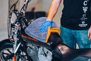 Hand drying black glossy Harley-Davidson motorcycle tank with a thick grey ADBL Dementor microfibre towel