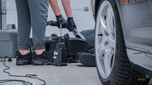A person cleaning a car with a vacuum and a black spray bottle on the floor 