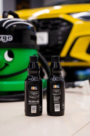 ADBL Pre-Spray Pro and Textile Rinse 0.5L bottles for a complete car upholstery cleaning system near a professional detailer's vacuum.