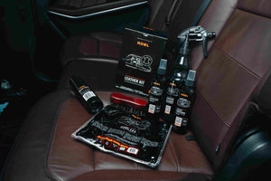 ADBL Leather Kit displayed on a brown car leather seat, showing bottles of cleaner, conditioner, foamer, brush, and kit box