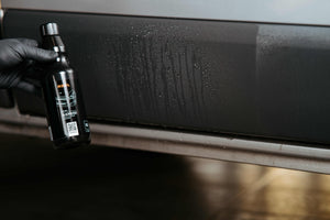 Hand holding ADBL Black Outer bottle next to a car's black plastic trim showing a clear before-and-after effect