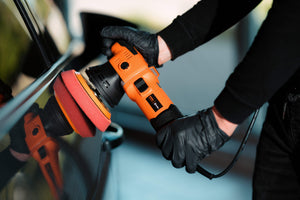 Detailer using ADBL Roller D15 Dual Action Polisher with red foam pad on a black car door/panel