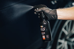 Hand in black glove spraying ADBL CERAMIC QD Quick Detailer onto a dark car body panel for shine