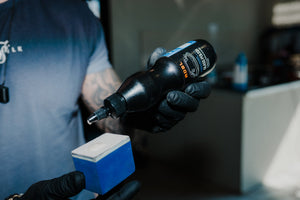 Person in black glove applying ADBL Glass Polish onto a blue foam applicator pad