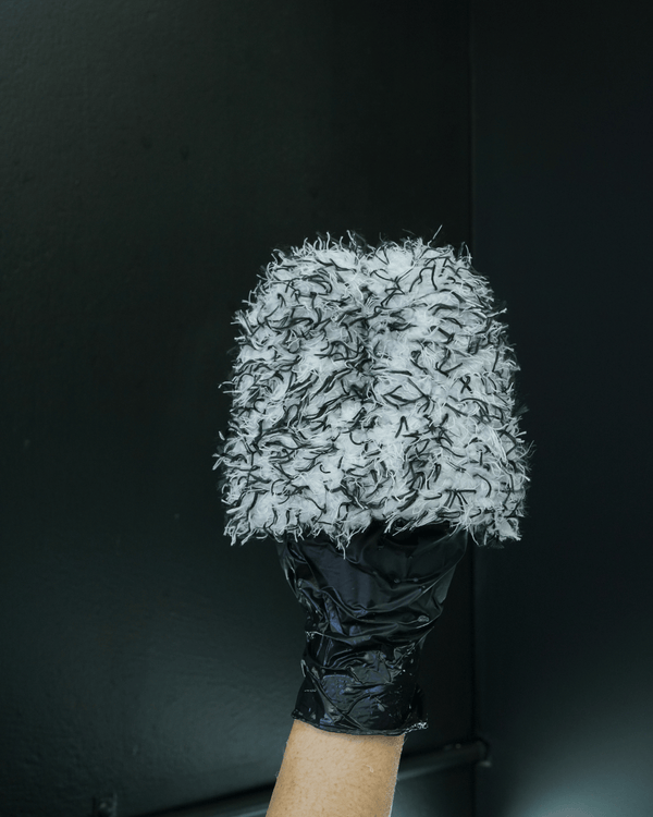 A person wearing black gloves holding a black and white wheel cleaning mitt