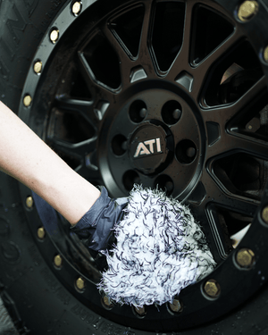 A person cleaning black rims with a black and white wheel cleaning mitt