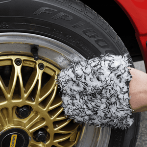 Person cleaning gold wheel with black and white wheel mitt