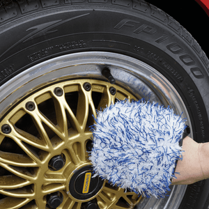 Person cleaning gold wheel with blue and white wheel mitt