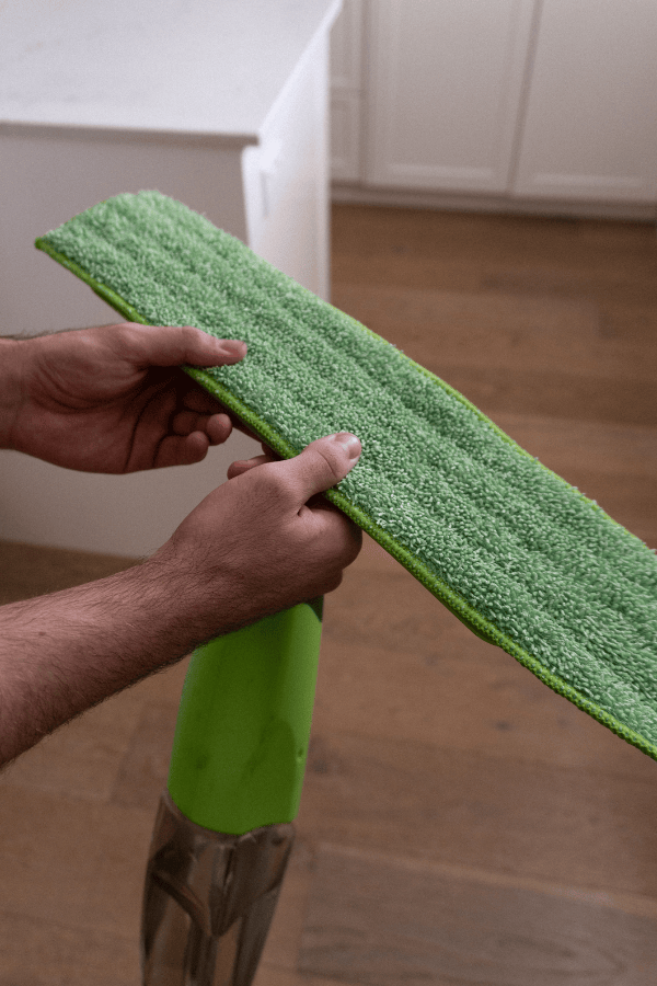A person using a green floor mop on a wood floor