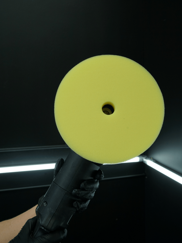 Yellow buffer pad held by a gloved hand against a dark background
