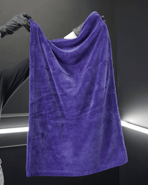 A person wearing black gloves holding a large blue microfibre drying towel in a detailing bay