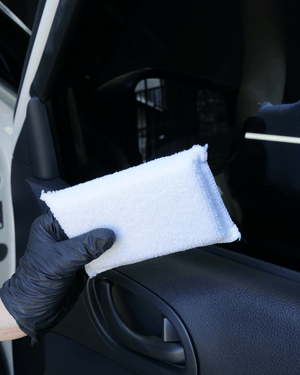 A person wearing black gloves holding a white interior applicator in front of a car door