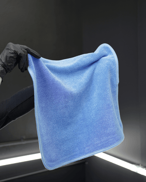 A person wearing black gloves holding a blue microfibre drying towel in a detailing bay