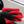 A person cleaning a white car with a red microfibre cloth and black gloves