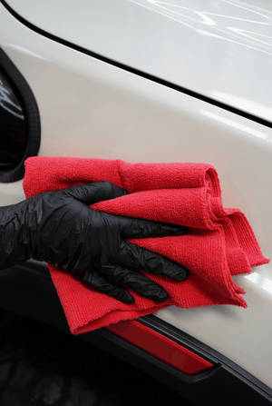 A person cleaning a white car with a red microfibre cloth and black gloves
