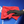 A person cleaning a blue car with a red microfibre cloth and black gloves on.