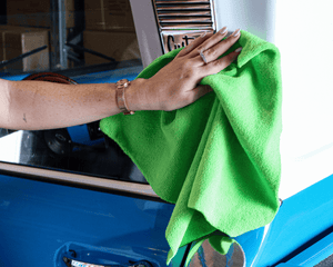 Person cleaning a blue vehicle with a green microfibre buffing cloth