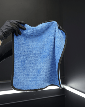 A person wearing black gloves holding a blue plush microfibre towel with a dark background 