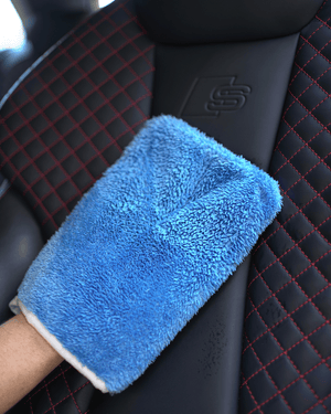 A person holding a blue car interior scrub mitt cleaning a leather car seat