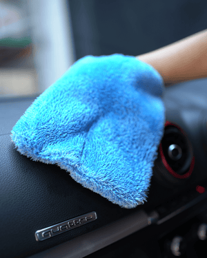 A person holding a blue interior scrub mitt cleaning a car dashboard