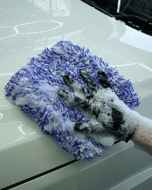 Person cleaning a car with a soapy glove and microfiber wash pad.