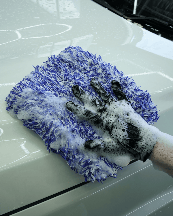 Person cleaning a car with a soapy glove and microfiber wash pad.