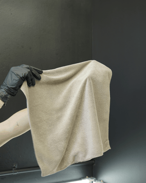 A person wearing black gloves holding a brown micrifbre cloth