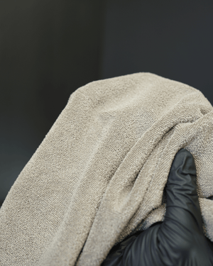 A person wearing black gloves holding a brown micrifbre cloth