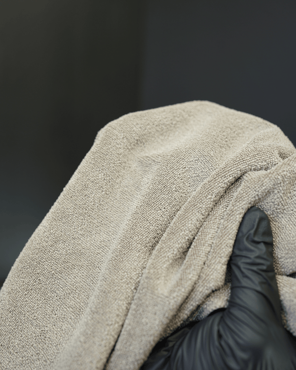 A person wearing black gloves holding a brown micrifbre cloth