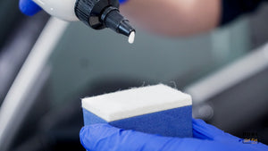 Hand in blue glove applying ceramic coating liquid product onto an ADBL Glass Cube Applicator sponge