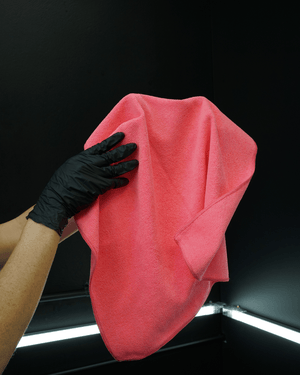 A person wearing a black glove holding a pink microfibre cloth 