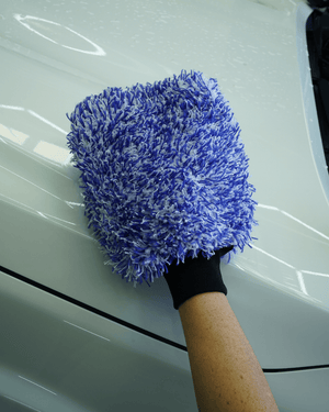 A person wearing a blue and white microfibre car wash mitt washing a whit ecar