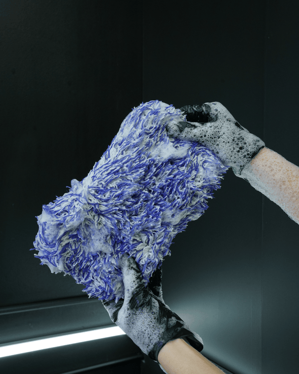 A person wearing black gloves holding a blue and white microfibre car wash mitt