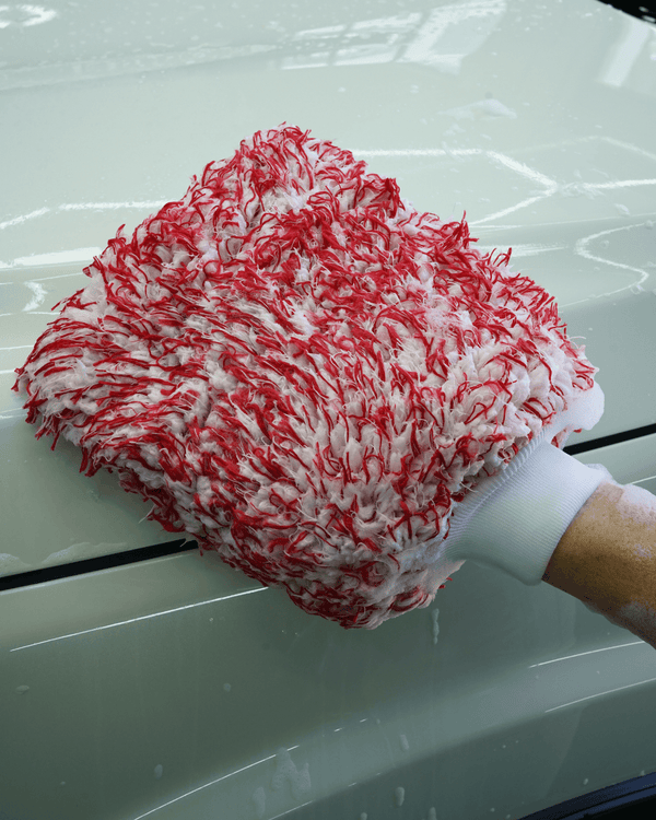 A person using a red and white wash mitt to clean a white car
