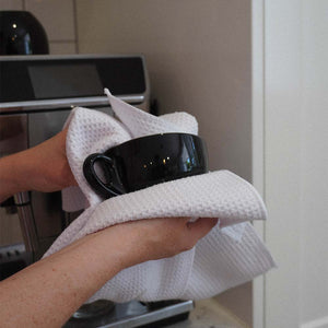 A person cleaning a black coffee cup with a white waffle weave cloth