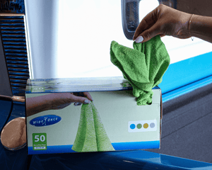 Person holding a green microfibre cloth above a box of Wipes-once cloths on a vehicle.