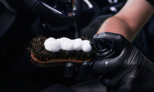 Detailer applying foam cleaning product onto a natural bristle brush for interior cleaning