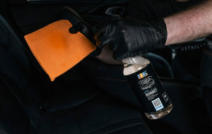 Person in black glove spraying ADBL BONNET cleaner onto an orange microfibre towel for interior spot cleaning