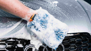 Hand in orange and blue ADBL PROMITT microfibre wash mitt applying thick foam on car grille