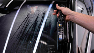 Hand spraying ADBL HYBRID GLASS Cleaner onto a wet car window for hydrophobic cleaning and protection