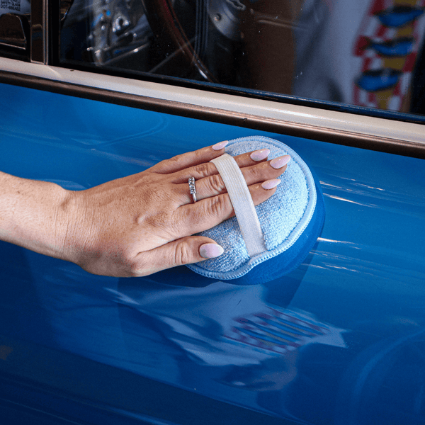 applicator with a strap being used on a blue car 