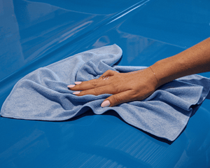 Hand holding a blue microfibre cloth on a blue surface